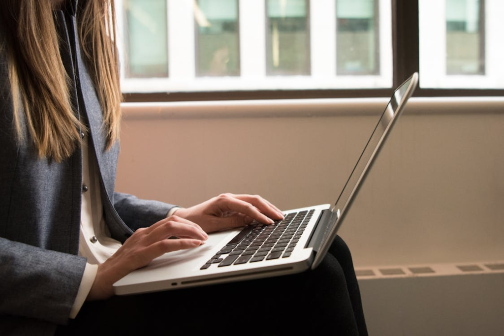 Professional woman in a blazer working on a laptop, reviewing academic documents and research materials.