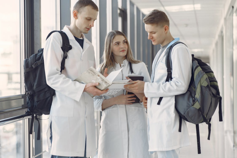 Three graduate students in lab coats reviewing research documents in a laboratory setting.