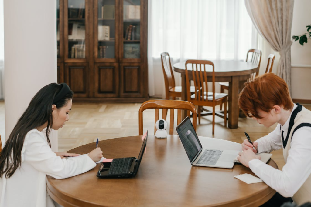 Two graduate students typing on laptops while collaborating on a thesis or academic project.