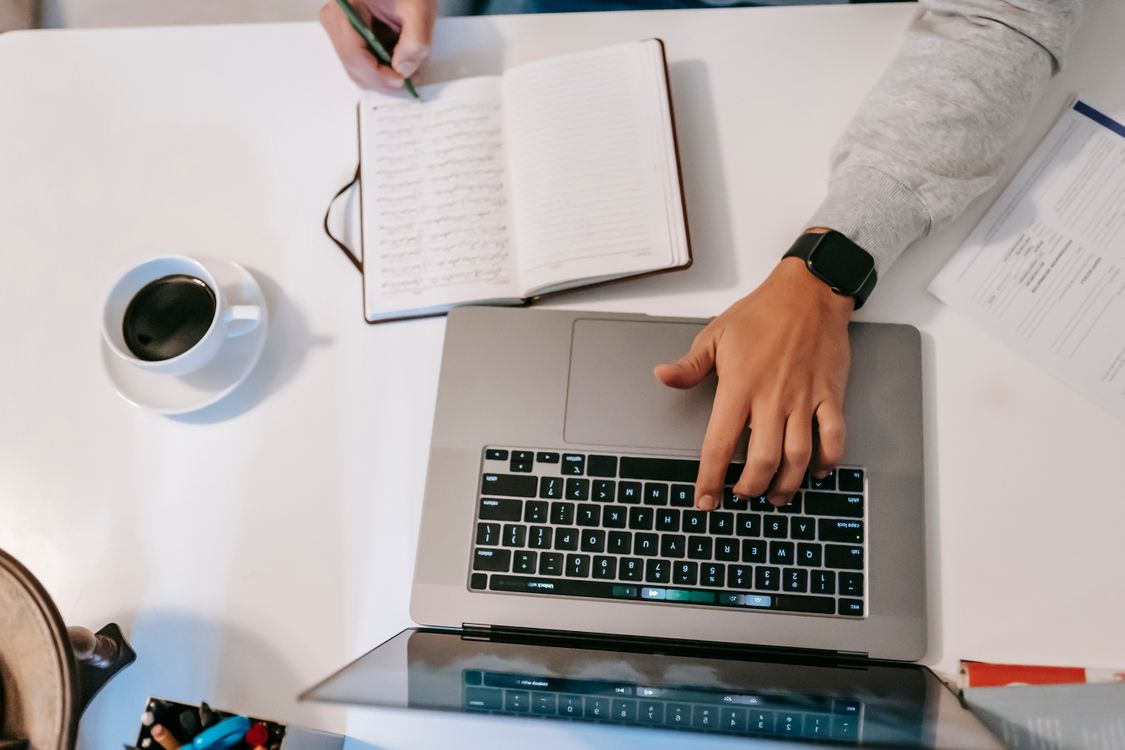 A person writes and researches on a laptop.
