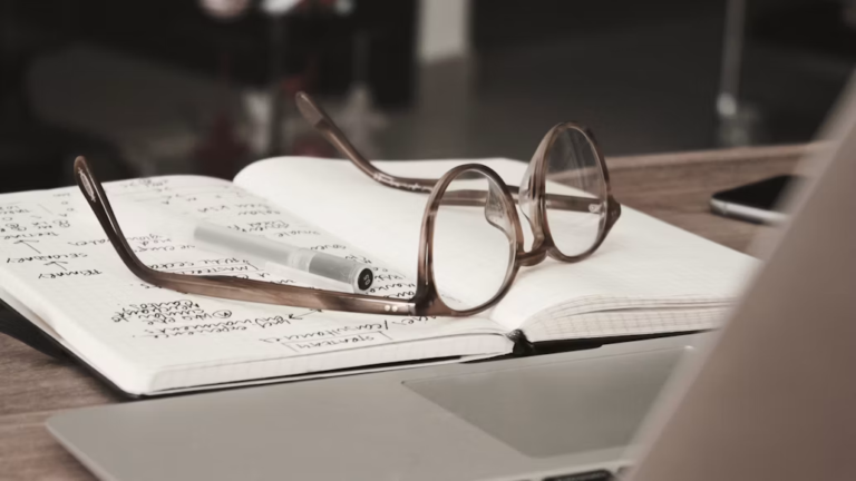 A notebook with research notes in it and glasses placed on top.